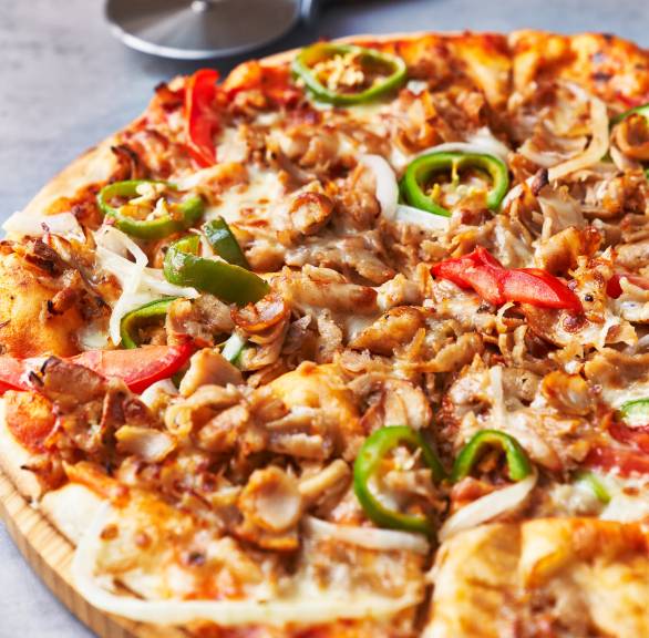 Runde Döner Pizza auf einem Pizzabrett, daneben ein Pizzaroller auf einem Tisch