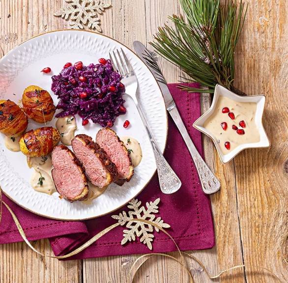 Entenbruststreifen mit Pancettakartoffeln und Rotkohl auf einem Teller, daneben Weihnachtsdeko