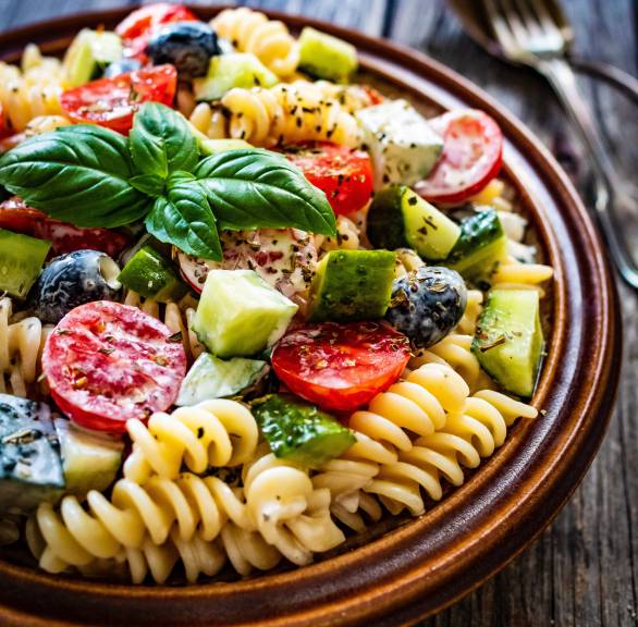 Pastasalat ohne Mayonnaise in einer Salatschüssel getoppt mit Basilikum und italienischen Kräutern