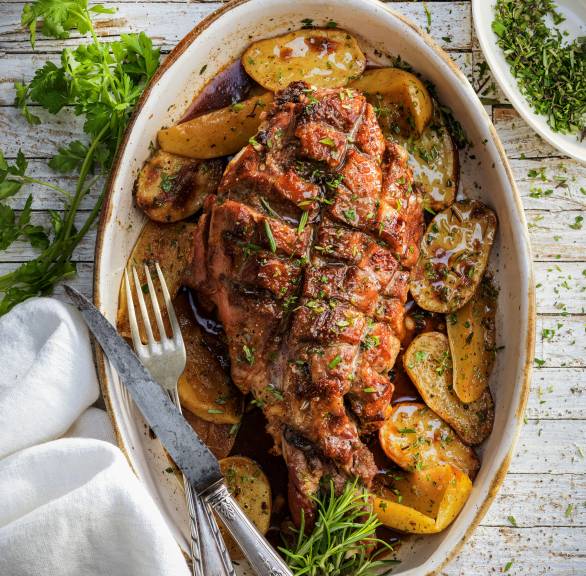 Spanferkel und Kartoffeln in einer Auflaufform dekoriert mit italienischen Kräutern auf einem Tisch