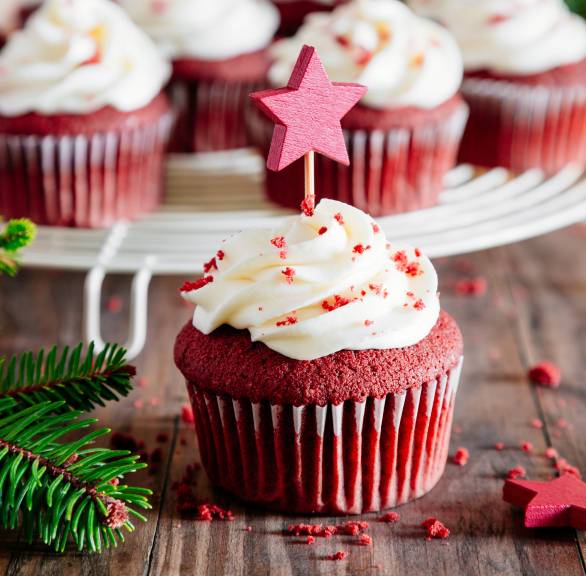 Red Velvet Weihnachtsmuffins mit Frischkäse-Topping auf einer Tortenplatte auf einem festlich dekorierten Tisch