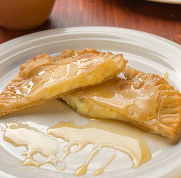 Seadas mit Käsefüllung halbiert auf einem Teller und mit Honig beträufelt