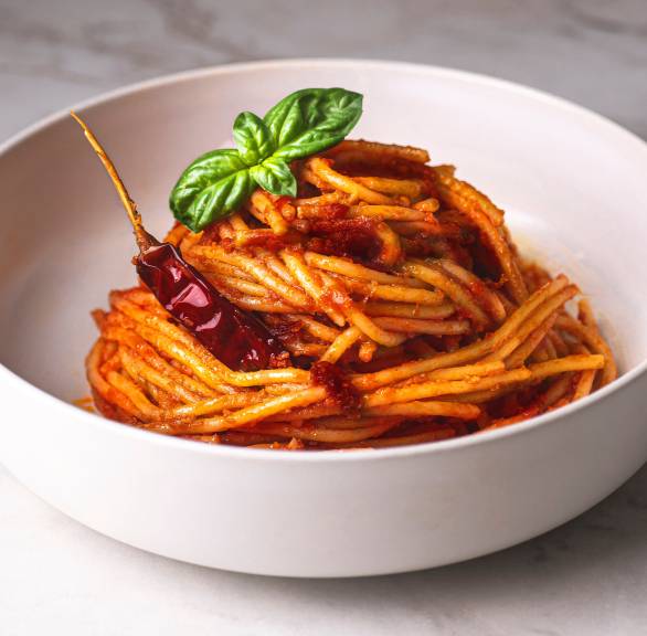 Spaghetti all’assassina in einer weißen Schale, getoppt mit einer getrockneten Chili und Basilikum