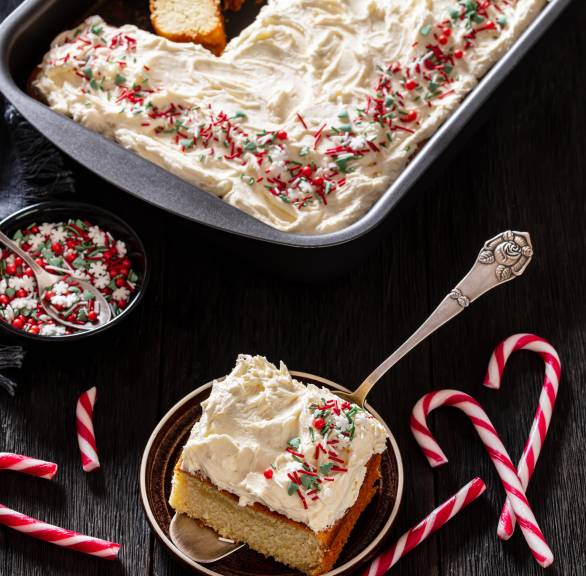 Angeschnittener Weihnachtskuchen auf einem Backblech, davor ein Stück auf einem Kuchenteller
