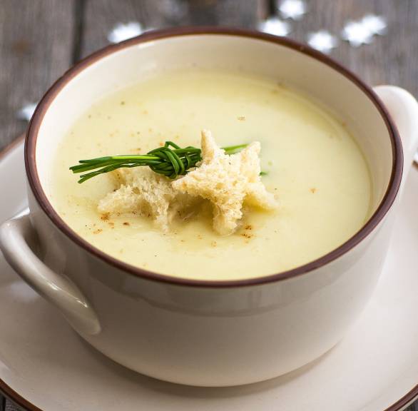 Weihnachtssuppe in einer Suppentasse getoppt mit Sternen aus Brot und Schnittlauch auf einem festlichen Tisch