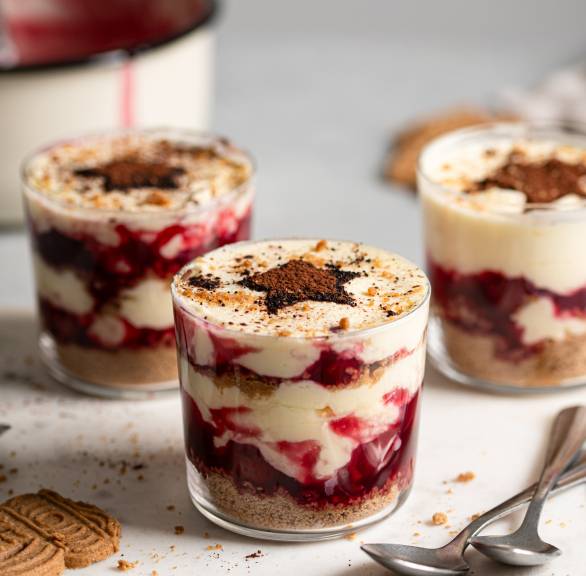Weihnachtstiramisu in drei Gläser gefüllt, daneben Spekulatius und Zimt auf einem Tisch
