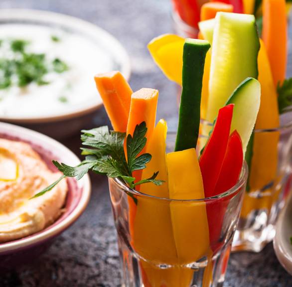 Gemüsesticks in zwei Gläsern, daneben eine Schale mit Dip