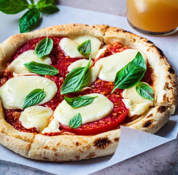 Runde vegane Pizza in Slices geschnitten auf einem Stück Backpapier garniert mit frischem Basilkum