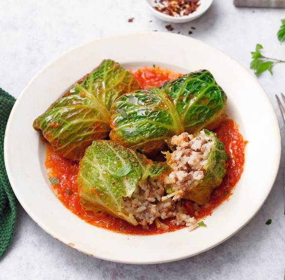 Vegane Wirsingrouladen in Tomatensauce auf einem Teller, daneben frische Kräuter