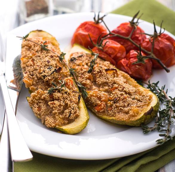 Vegane Zucchinischiffchen mit Amaranthfüllung auf einem Teller getoppt mit italienischen Kräutern