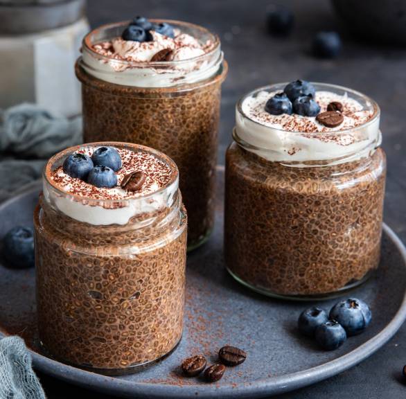 Veganer Chiapudding mit Espresso in drei Weckgläsern auf einem Tablett dekoriert mir Blaubeeren und Espressobohnen