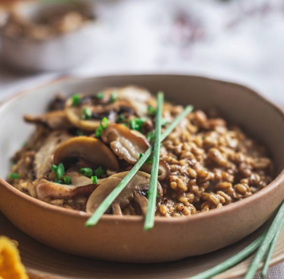 Veganes Hafer-Risotto mit Pilzen in einer Tonschale garniert mit frischen Kräutern