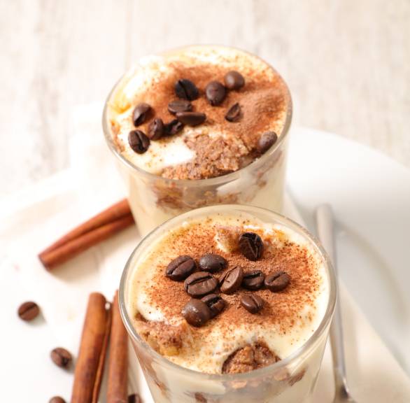 Veganes Weihnachtstiramisu in zwei Dessertgläsern dekoriert mit Zimtstangen und Sternanis auf einem Tisch