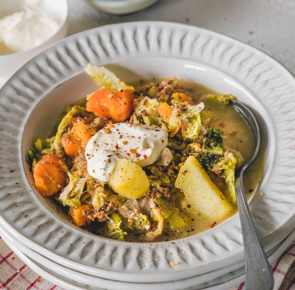 Wirsingeintopf mit veganem Hackfleisch in einem Suppenteller getoppt mit veganer Crème fraîche