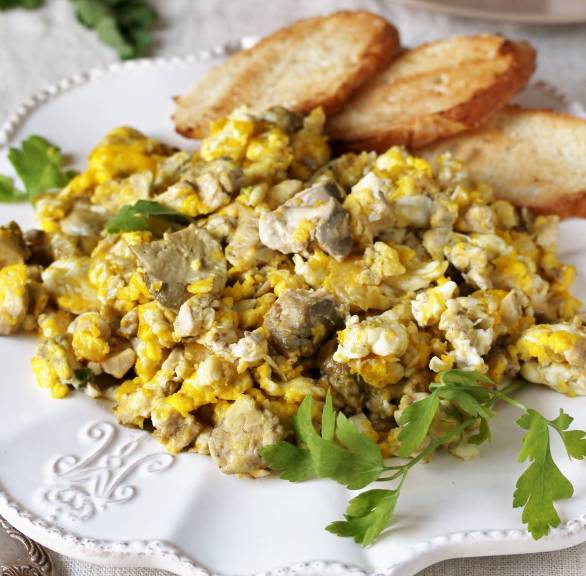 Agnello Cacio e Uova Rührei mit Lamm und Käse auf einem weißen Teller, daneben geröstete Brotscheiben