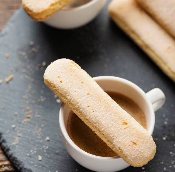 Selbst gebackene Löffelbiskuits auf einer Schieferplatte mit einer Tasse Espresso