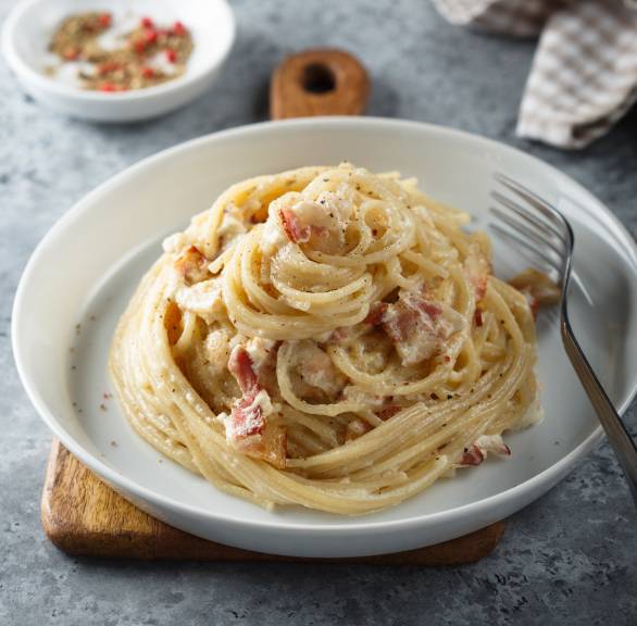 Spaghetti Carbonara als Türmchen auf einem weißen Teller, daneben Parmesan auf einem Tisch