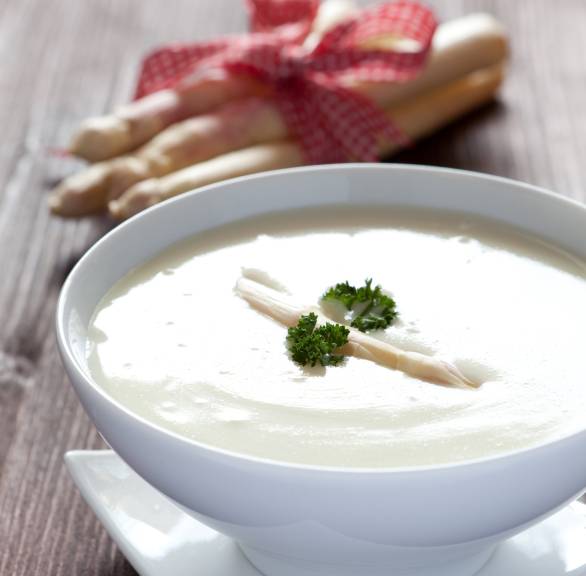 Spargelcremesuppe in einer Suppenschüssel, dahinter weißer Spargel