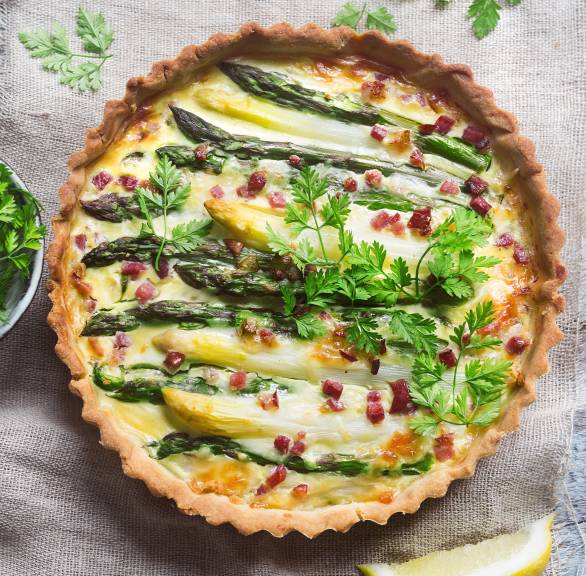 Runde Spargelquiche mit weißem und grünem Spargel mit Schinkenwürfeln auf einem frühlingshaft dekorierten Tisch