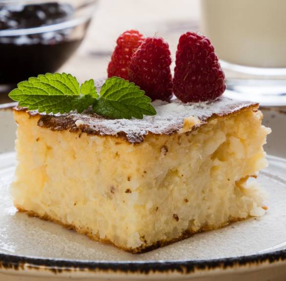 Ein Stück Torta di Riso Reiskuchen auf einem Kuchenteller bestäubt mit Puderzucker und dekoriert mit Himbeeren und Minze
