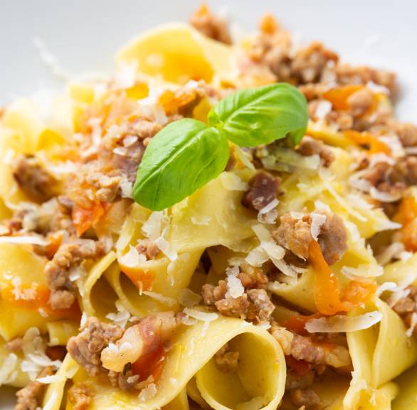 Weiße Bolognese mit Pappardelle auf einem tiefen, weißen Teller dekoriert mit frischem Basilikum