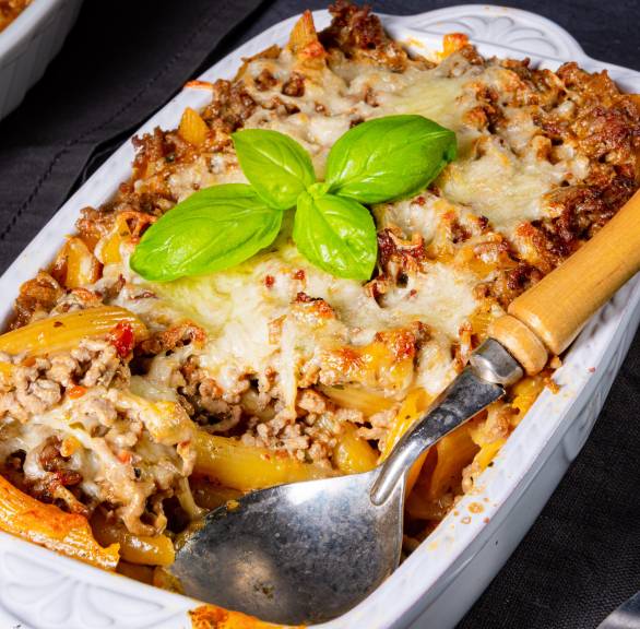 Bolognese-Auflauf in einer weißen Auflaufform mit Schichten aus Hackfleischsoße und Penne mit Käse gratiniert auf einem Tisch