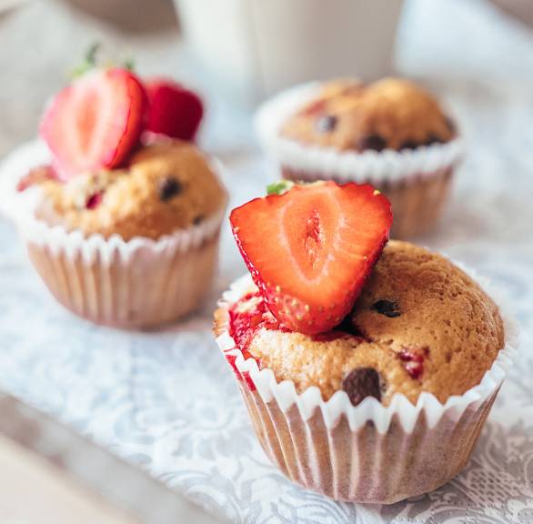 Drei Erdbeer-Muffins dekoriert mit einer halben Erdbeere auf einem Küchentisch