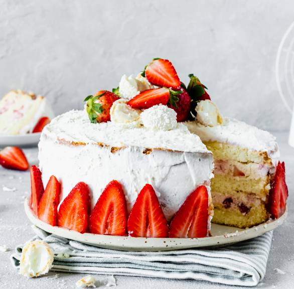 Erdbeer-Raffaello-Torte angeschnitten auf einer Tortenplatte dekoriert mit Mascarponecreme und frischen Erdbeeren