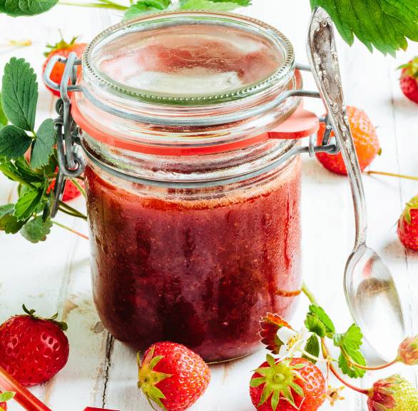 Erdbeer-Rhabarber-Marmelade in einem geschlossen Weckglas auf einem Holztisch, daneben Erdbeeren und Rabarberstücke