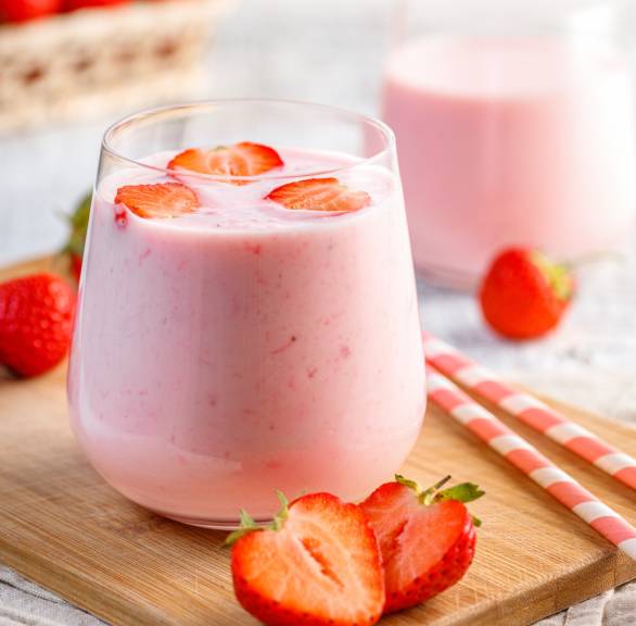 Erdbeer-Smoothie in zwei Gläser gefüllt und mit frischen Erdbeerstücken garniert auf einem Holzbrett