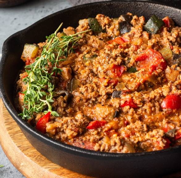 Gemüsebolognese mit Hackfleisch, Paprika, Zucchini und Oliven in einer Pfanne garniert mit frischen Kräuter
