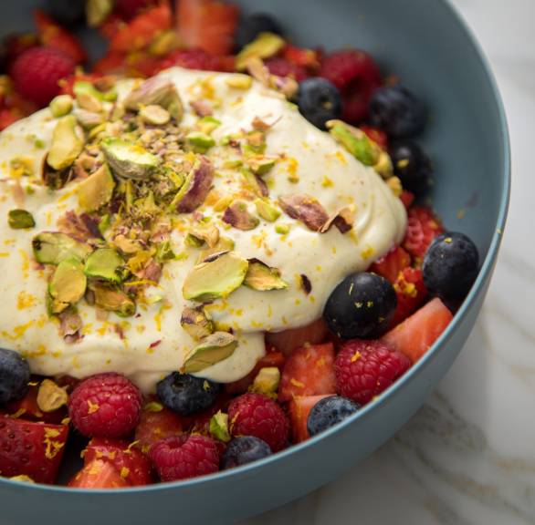 Obstsalat aus Beeren mit Leinöl-Quark-Creme in einer grauen Schale getoppt mit Zitronenabrieb und Pistazien