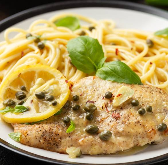 Piccata alla milanese: Panierte Kalbsschnitzel auf einem Teller mit Spaghetti, darüber Weißwein-Zitronen-Sauce, Kapern und Basilikum