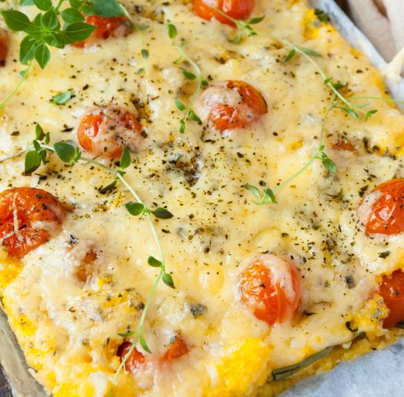 Polenta-Auflauf mit Tomate Mozzarella auf einem Küchentisch garniert mit frischen Kräutern