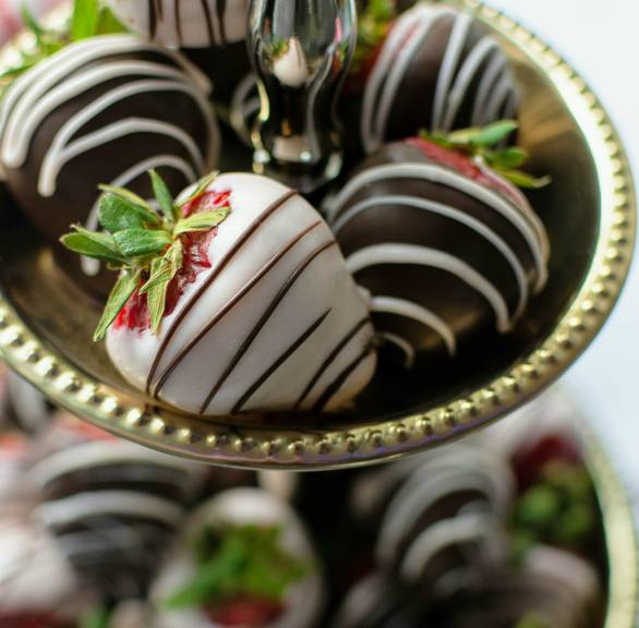 Helle und dunkle Schoko-Erdbeeren mit Grün angerichtet auf einer silbernen Etagere
