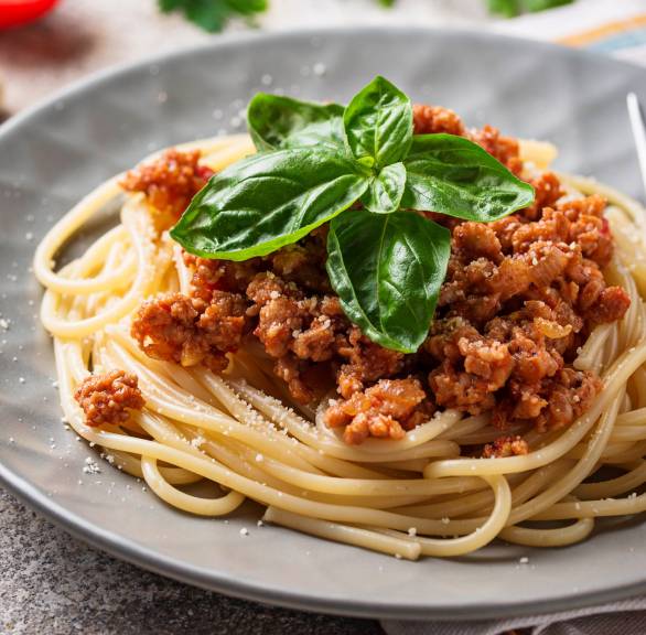 Spaghetti mit Bolognese-Soße auf einem runder Teller getoppt von frischem Basilikum