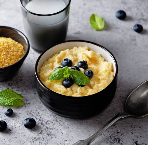 Süße Polenta in einer Schale getoppt mit Blaubeeren und Minze, daneben Maisgrieß