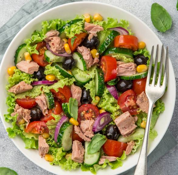 Thunfischsalat mit Mais, Oliven, Gurke, Zwiebel und Tomate auf einem Teller garniert mit frischer Petersilie