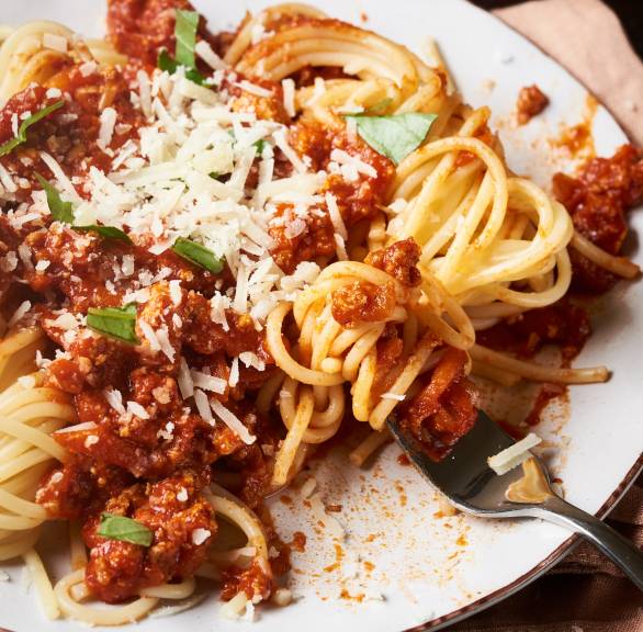 Spaghetti mit veganer Tofu-Bolognese auf einem Teller getoppt mit Hefeflocken und Basilikum