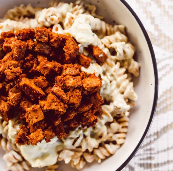 Fusilli Pasta mit veganer Carbonara-Soße getoppt mit Speck aus Tempeh in einer Schüssel