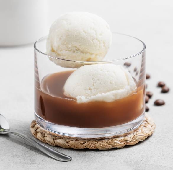 Affogato al Caffè: Eine Kugel Vanilleeis in einem Glas übergossen mit Espresso, dahinter ein Kännchen