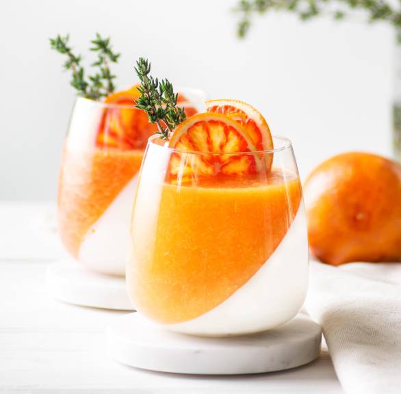 Aperol Spritz Panna Cotta in zwei Gläsern, eine Schicht Panna Cotta eine Schicht Aperol-Fruchtmasse dekoriert mit thymianzweigen 