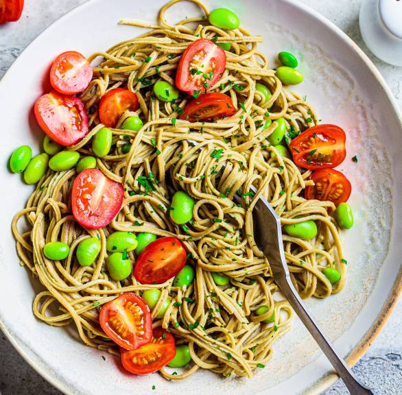 Edamame-Spaghetti auf einem Teller getoppt mit Kirschtomaten und Edamame-Bohnen sowie frischer Petersilie