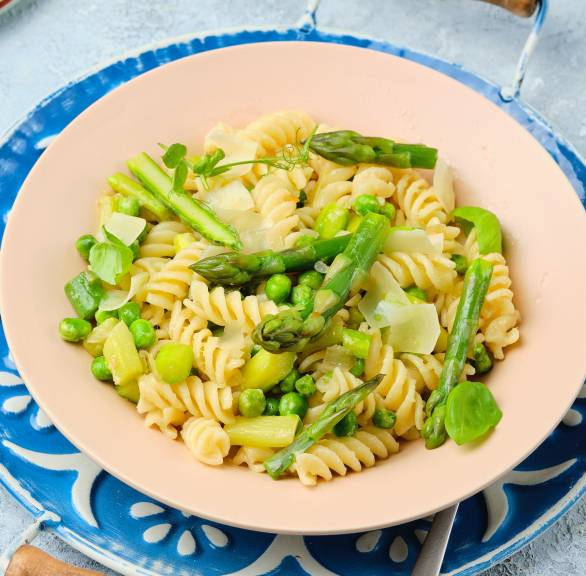 Pasta alla Primavera aus Fusilli, grünem Spargel und Erbsen in Sahnesauce auf einem Teller, darunter ein Platzteller mit Mosaik