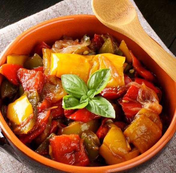 Peperonata italienisches Schmorgericht aus Paprika in einer Pfanne, drumherum bunte Paprikaschoten