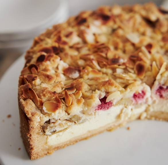Runder Quark-Rhabarber-Kuchen angeschnitten auf einer Kuchenplatte im close up