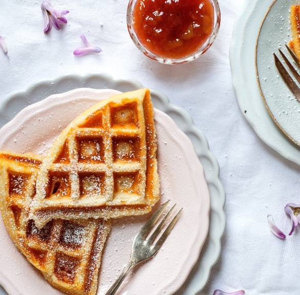 Zerteilte Quark-Waffeln auf zweit Tellern, daneben ein Glas Rhabarberkompott auf einem Tisch