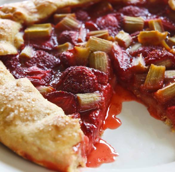 Rhabarber-Ricotta-Crostata mit Erdbeeren angeschnitten auf einem Teller, Saft des Obstes fließt heraus