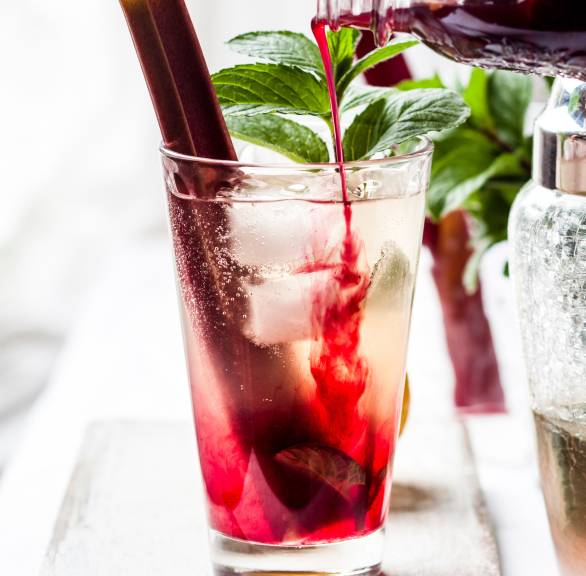 Für Rhabarber-Spritz wird Rhabarbersaft in ein Aperitif-Glas mit Eiswürfeln geschüttet, garniert mit frischer Minze