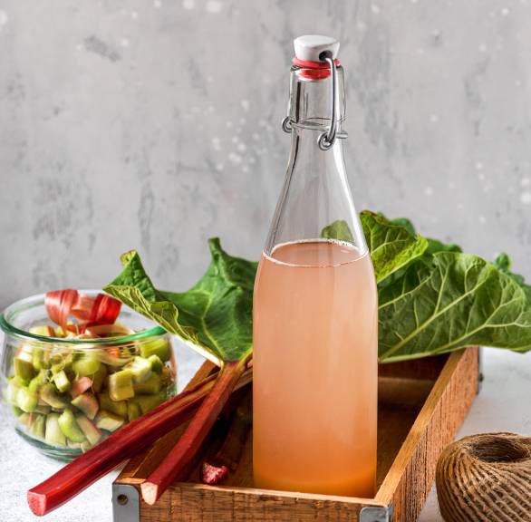 Selbst gemachter Rhabarbersirup abgefüllt in eine Flasche in einer Holzkiste auf einem Tisch